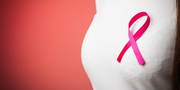 Healthcare, medicine and breast cancer awareness concept - Closeup of pink badge ribbon on woman chest to support breast cancer cause on red