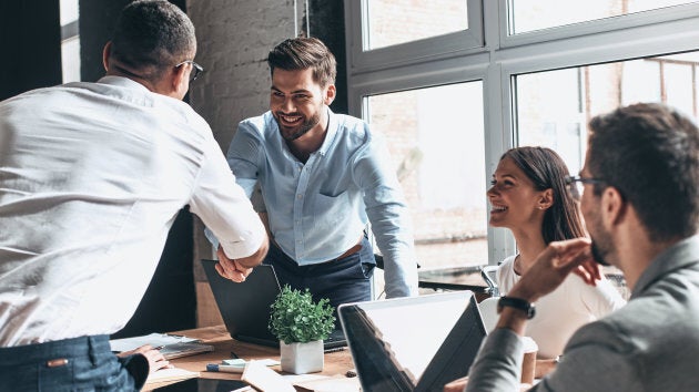 Young modern men in smart casual wear shaking hands and smiling while working in the creative office