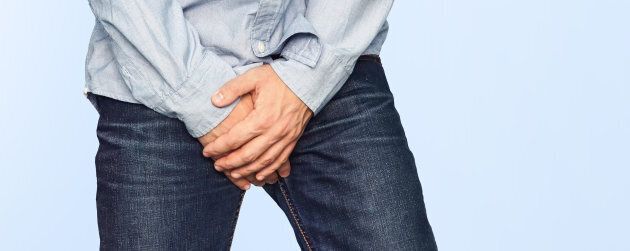 Close up of a man with hands holding his crotch on a light blue background. Urinary incontinence. Men's health. The pain from the blow in groin.