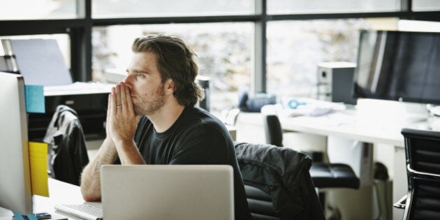 Businessman with hands on chin sitting at office workstation looking at computer monitor