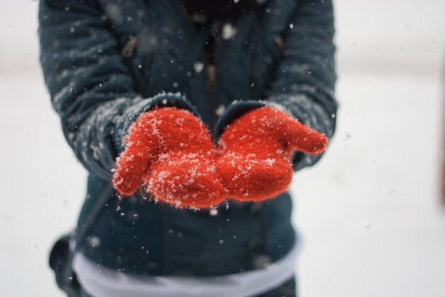 Girl catching snowflakes which are falling on her orange knitted gloves.