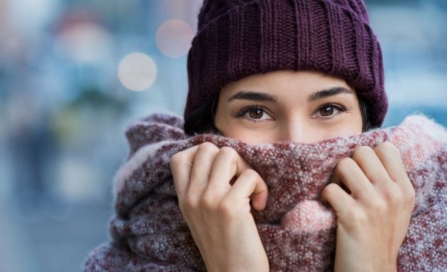 Winter portrait of young beautiful woman covering face with woolen scarf. Closeup of happy girl feeling cold outdoor in the city. Young woman holding scarf and looking at camera.'r