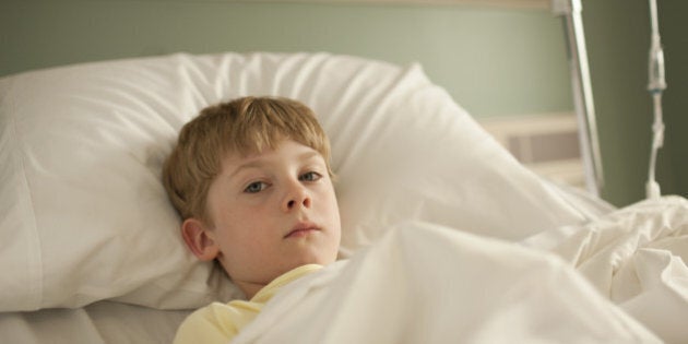 Young boy lying in hospital bed looking at camera with sad
