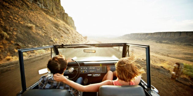 Young couple driving convertible off road vehicle at sunset on desert road