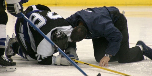 An injured hockey player is attended to on the ice by the team doctor.