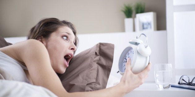 Upset woman holding her alarm clock with an expression of fright