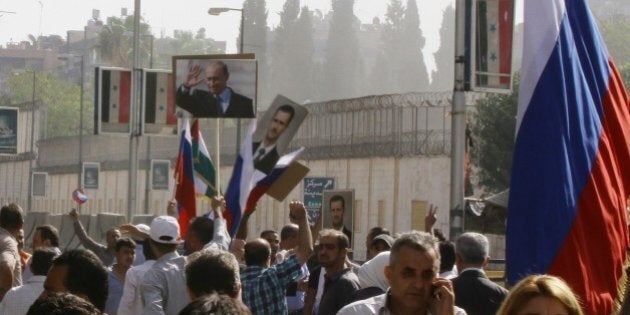 Several hundred people, holding up Russian and Syrian flags as well as portraits of the two countries' presidents, gather near the Russian embassy in Damascus on October 13, 2015 to express their support for Moscow's air war in Syria, just before two rockets struck the embassy compound sparking panic among the crowd. AFP PHOTO/LOUAI BESHARA (Photo credit should read LOUAI BESHARA/AFP/Getty Images)