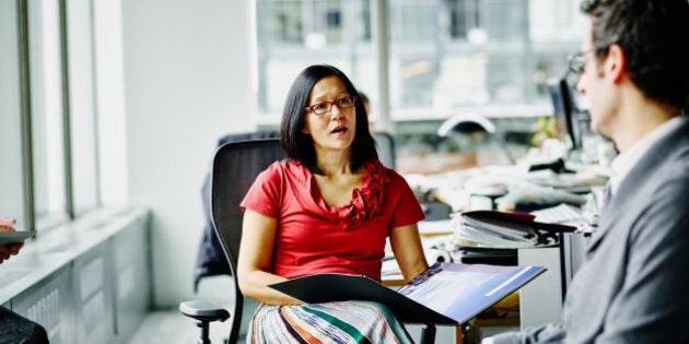 Businesswoman leading informal meeting with colleague at workstation in office