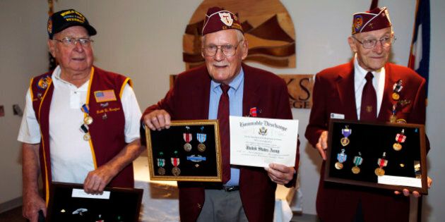 John Pederson, center, holds up his medals as well as his honorable discharge certificate as fellow veterans Keith Hereford, left, and Clayton Nattier look on Thursday, July 2, 2015, following a ceremony in Lakewood, Colo. The three Colorado veterans, who were captured by the German military in World War II, received their decorations more than 70 years after they were liberated. (AP Photo/David Zalubowski)