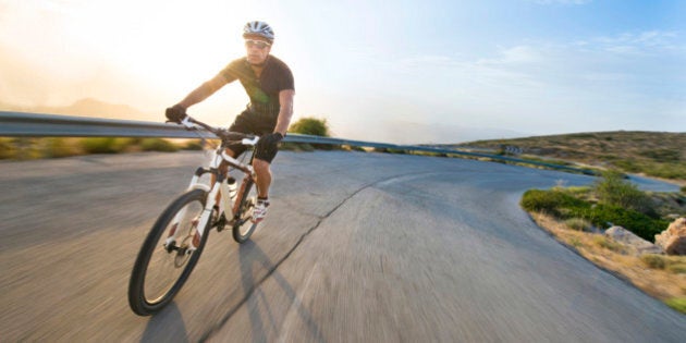 Cyclist man riding mountain bike in sunny day on a mountain road. Image with flare.