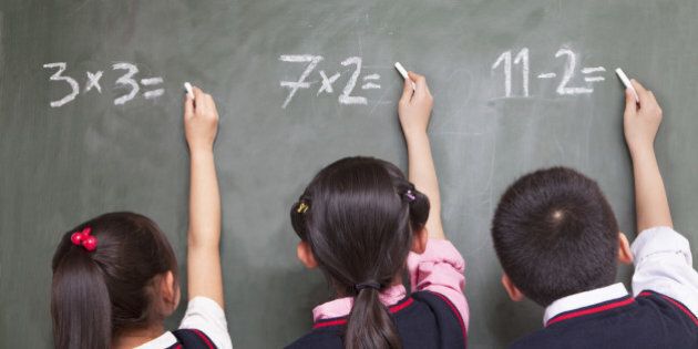 Three school children doing math equations on the blackboard
