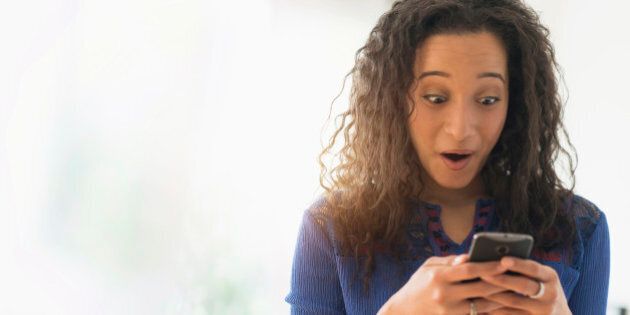 Close up of mixed race woman gasping at cell phone