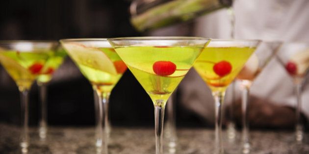 Appletini cocktails ready to be served garnished with apple slices and maraschino cherries with a bartender pouring drinks in the background at a holiday party, Manhattan, New York City, New York, United States, North America.