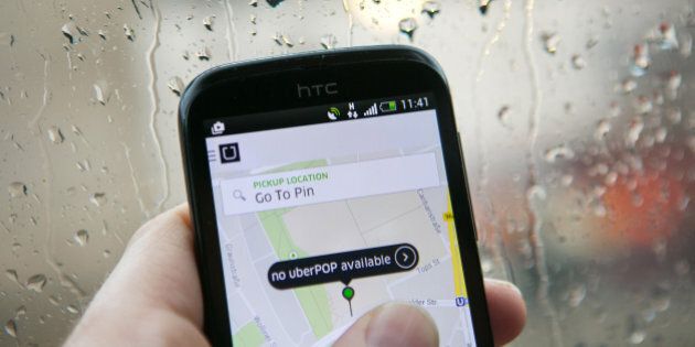 A HTC Corp. smartphone displays the Uber Technologies Inc. UberPop car service application (app) as rain streaks an automobile windshield in this arranged photograph in Berlin, Germany, on Monday, Nov. 24, 2014. Uber is reducing the number of vehicles operating in two German cities during non-peak hours as the car-sharing service struggles with legal challenges that have forced it to lower prices. Photographer: Krisztian Bocsi/Bloomberg via Getty Images