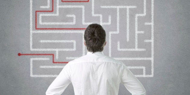 Confused young businessman looking at the labyrinth on the wall