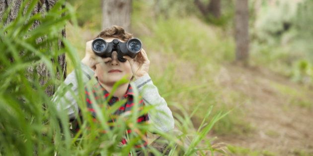 Young boy looking through binoculars in tall grass