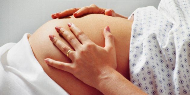 Pregnant woman in hospital gown rubs belly