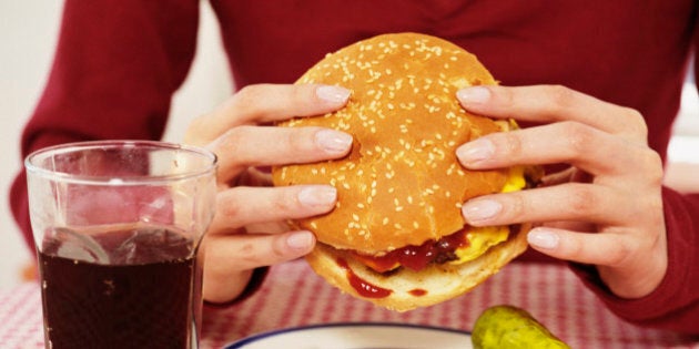 Woman holding cheeseburger, soft drink beside plate, close-up