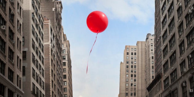 Red balloon floating through city