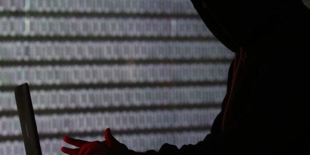 An illuminated wall displays a stream of binary coding, text or computer processor instructions, as a man is seen profiled in silhouette whilst working on a laptop computer in this arranged photograph in London, U.K., on Wednesday, Dec. 23, 2015. The U.K.s biggest banks fear cyber attacks more than regulation, faltering economic growth and other potential risks, and are concerned that a hack could be so catastrophic that it could lead to a state rescue, according to a survey. Photographer: Chris Ratcliffe/Bloomberg via Getty Images