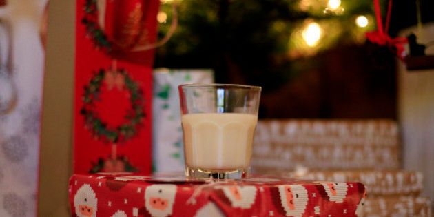 A glass of milk rests on presents underneath a Christmas tree.