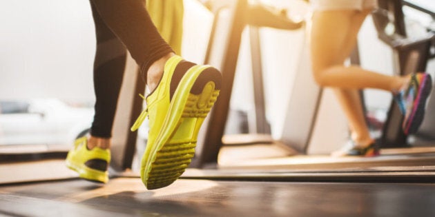 Two unrecognizable people exercising on treadmill in a health club.