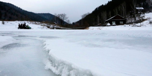 People drive on a snowmobile across the frozen Bolshaya Listvenka river in the Siberian Taiga district outside Krasnoyarsk, December 7, 2014. REUTERS/Ilya Naymushin (RUSSIA - Tags: SPORT TRAVEL SOCIETY ENVIRONMENT)