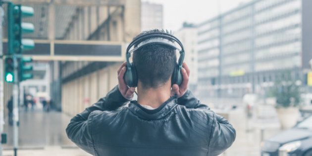Back view of a young man with headphones listening to music in the city streets