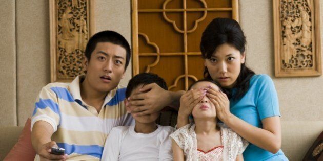 Family watching television with parents covering children's eyes
