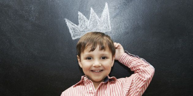 Studio shot of an adorable little boy with a drawing of a crown on a blackboard behind him