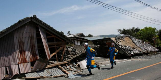 Police officers run in front of collapsed houses in Mashiki, Kumamoto prefecture, southern Japan, Friday, April 15, 2016. Aftershocks rattled communities in southern Japan as businesses and residents got a fuller look Friday at the widespread damage from an unusually strong overnight earthquake. (AP Photo/Koji Ueda)