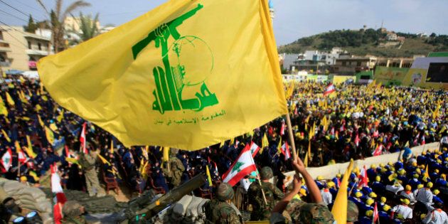 A Hezbollah fighter waves its flag as other fighters stand guard during a rally commemorating