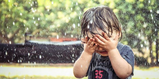 A photo of a young boy being caught in a rain shower and covering his face with his hands