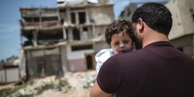 A Palestinian man carrying a child walks past buildings destroyed during the 50-day war between Israel and Hamas-led militants in the summer of 2014, on April 30, 2016, in Gaza City.Reconstruction aid to over 1,000 families in Gaza has been suspended due to a lack of materials, the United Nations said on April 28, after Israel banned the private import of cement over corruption claims. / AFP / MAHMUD HAMS (Photo credit should read MAHMUD HAMS/AFP/Getty Images)