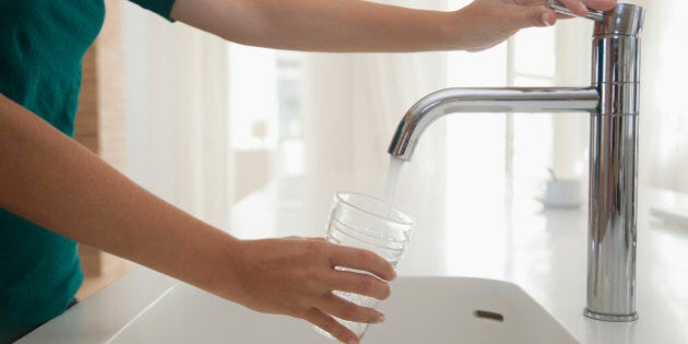 Woman filling glass of water at kitchen sink, cropped