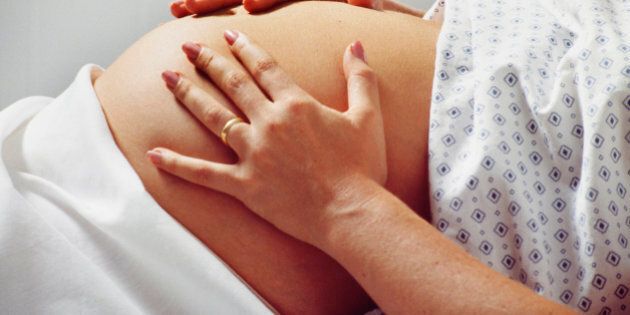 Pregnant woman in hospital gown rubs belly