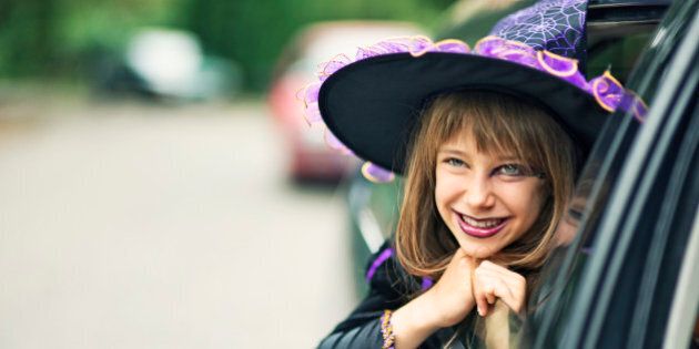 Portrait of a little girl during halloween dressed up as a witch. The girl is aged 9 and is smiling from the car window. Street visible in the background and a lot of nice copy space.
