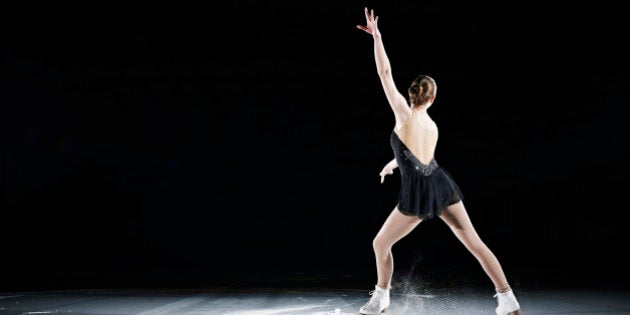 Female figure skater performing on ice rink in arena rear view