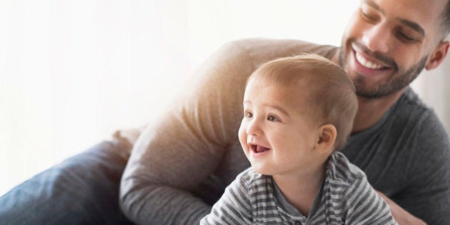 Smiling father playing with baby son on bed