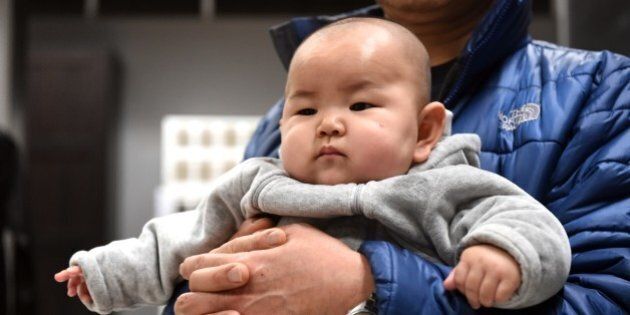 This picture taken on January 19, 2015 shows a Chinese baby in the arms of his father at a furniture store in Beijing. China's working-age population continued to fall in 2014, the government said on January 20, as Beijing struggles to address a spiralling demographic challenge made worse by its one-child policy. AFP PHOTO/GOH CHAI HIN (Photo credit should read GOH CHAI HIN/AFP/Getty Images)