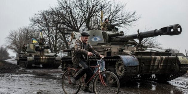 A local resident rides a bicycle as Ukrainian servicemen sit atop an armoured vehicle with Ukrainian flags, on the outskirts of Donetsk, Ukraine, Wednesday, March 4, 2015. Fighting has waned substantially in eastern Ukraine in recent days as a cease-fire deal forged last month increasingly takes effect, but both sides have complained of sporadic violations. (AP Photo/Evgeniy Maloletka)