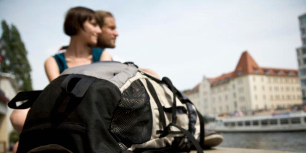 A backpack and a young couple by the Spree river, Berlin, Germany, focus on backpack