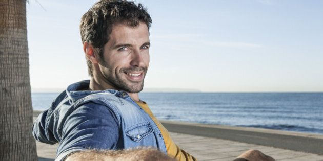 Spain, Mid adult man sitting on bench, smiling, portrait