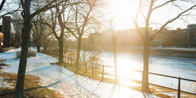 This is a horizontal, color, royalty free stock photograph of ice frozen on the pathway of Lachine Canal a National Historic site in Montreal an urban travel destination in Quebec, Canada. The bright afternoon sun casts a lens flare across the urban scene with no people. Photographed with a Nikon D800 DSLR camera.