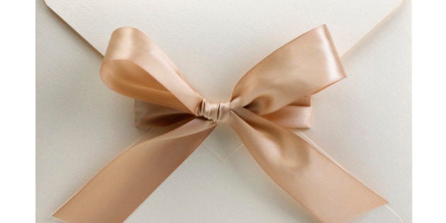 White envelope with bow, containing a wedding invitation. This is a macro photograph and its frame is square.