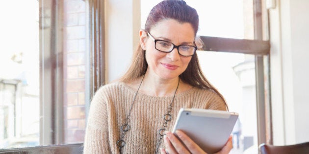 Senior woman working on digital tablet in cafe.