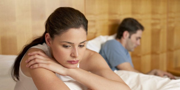 Bored woman sitting in bed with man using laptop by her