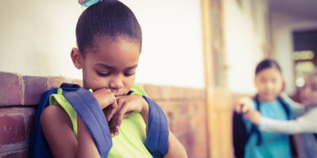 Sad pupil being bullied by classmates at corridor in school