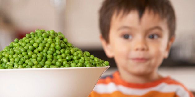 Young boy in kitchen with a bowl of green peas