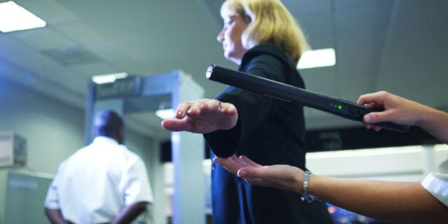 Close-up of an airport security officer using a hand held metal detector to check a traveler
